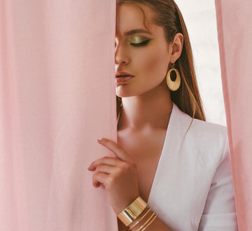 Woman wearing gold earrings and bracelet against a pink curtain